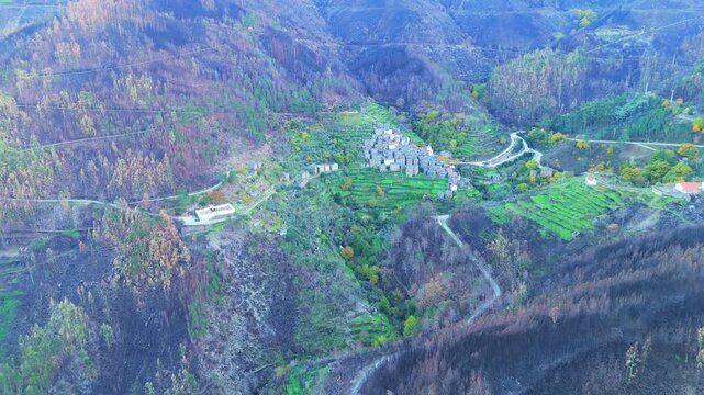 Piodao historic schist village in autumn and Serra do Acor mountain slope with lush green and burned vegetation scorched by forest fires. Distant Shot. Central Portugal. Aerial view. Moving Forward