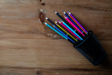 Top view of colored pencils in fallen pen holder on wooden desk.