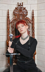 Beautiful redhaired woman warrior with sword sitting on the throne shows strength fantasy