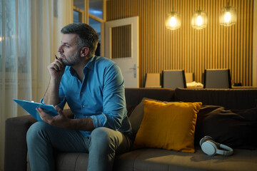 Mature man thinking and generating ideas in the living room in the evening