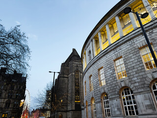 Curved neoclassical building in Manchester city center with illuminated columns and ferris wheel