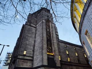 Old stone church tower in Manchester, UK, illuminated at dusk with modern nearby structures