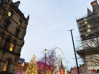 Manchester city centre at dusk with festive lights, Christmas tree, and a large Ferris wheel