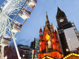 Giant Ferris wheel beside illuminated Gothic church in Manchester city centre UK at dusk tonight