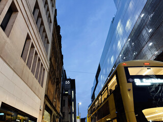 Urban street scene in Manchester at dusk with a yellow tram and modern glass building