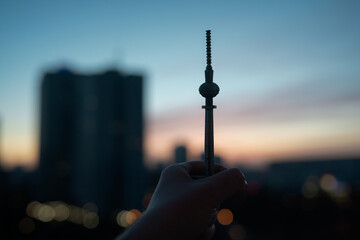 Silhouette Of A Hand Holding A Decorative Television Tower Against City Sunset And Modern Skyline