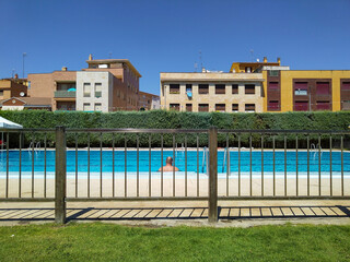 Public swimming pool viewed through a fence in summer