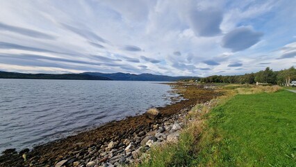 A fjord in Fauske, Norway, framed by rugged mountains and calm waters, is particularly striking in autumn. The surrounding slopes are painted in shades of gold, red, and orange as the deciduous trees 