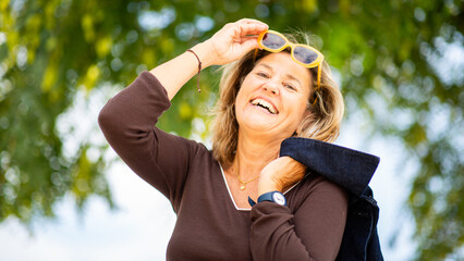 Cheerful mature woman laughing with yellow sunglasses in hand
