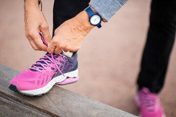 Close-up of woman tying pink running shoes on a wooden bench