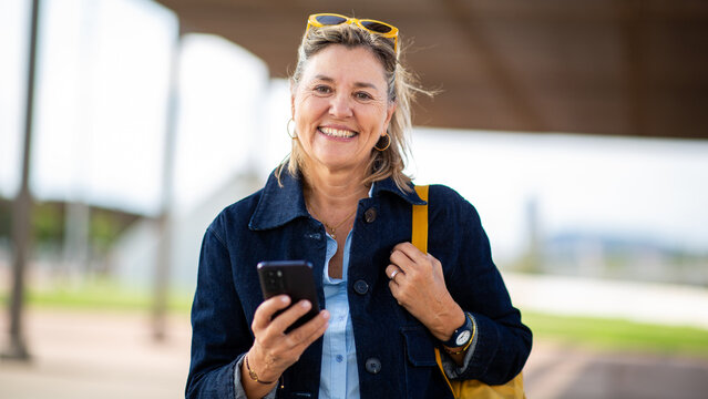 Smiling mature woman holding smartphone and looking at camera