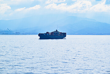 Silhouette of a cargo ship at sea against a blue sky on the horizon