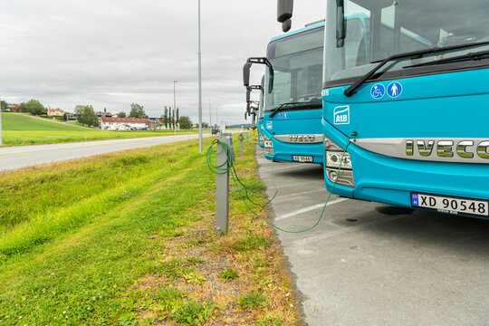 26 july 2025, Levanger, Norway. Row of electric public busses, atb, front view, charging at a charging station. Charging electicity cable is visible and connected, plugged into the socket of the bus.