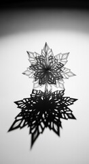 Obraz premium Intricate paper snowflake casting a dramatic shadow on a white surface.