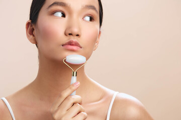 asian woman uses facial roller in a skincare routine, close up shot with soft lighting, calm expression and clean aesthetic, serene spa vibe, minimal background, healthy glow and selfcare mood. © SHOTPRIME STUDIO