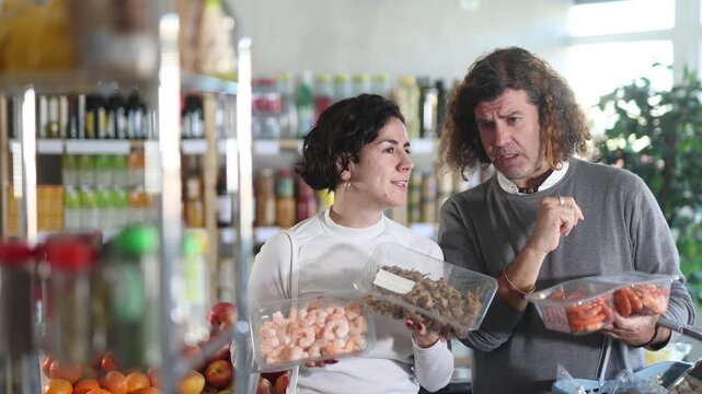 Husband and wife consult which shrimp to buy. European pair chooses large shrimps and mollusks Bolinus brandaris in the supermarket. High quality 4k footage