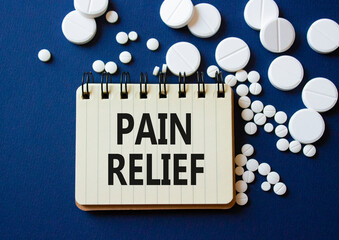 Pain Relief symbol. Concept word Pain Relief on notebook. Beautiful deep blue background with pills. Medicine and Pain Relief concept. Copy space