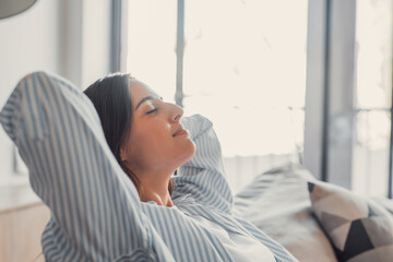 Relaxed serene pretty young woman feel fatigue lounge on comfortable sofa hands behind head rest at home, happy calm lady dream enjoy wellbeing breathing fresh air in cozy home modern living room
