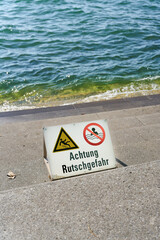 Warnschild mit der Aufschrift Achtung Rutschgefahr an den Treppenstufen der kleinen Seemole am Bodensee in Bregenz