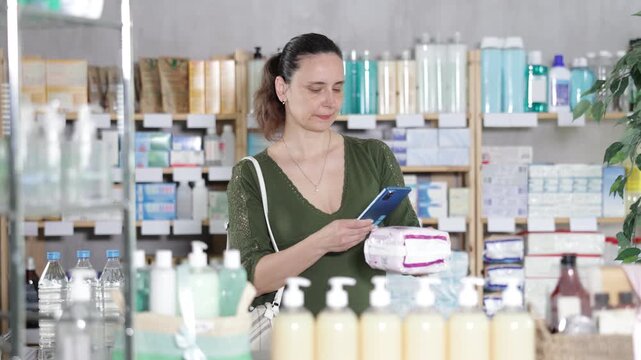 Woman in pharmacy scans QR code on feminine pads, uses quick link to access drugs instructions. Client wants to make sure of quality of product