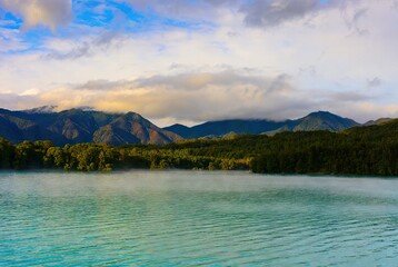 A serene morning mist rising over the tranquil turquoise lake with majestic mountains and dense forest