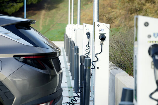 Parte trasera de un coche el&eacute;ctrico enchufado a puntos de carga urbanos para cargar la bater&iacute;a, movilidad sostenible cero emisiones