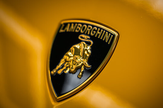 Tight close up of the Lamborghini crest on a yellow panel, gold bull and Lamborghini lettering on a black shield in controlled lighting with shallow depth of field.