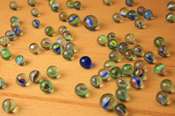 Bunte Glasmurmeln mit farbigen Wirbeln liegen verstreut auf Holz. Eine dunkelblaue Vollmurmeln hebt sich deutlich ab und symbolisiert Individualität inmitten der Vielfalt.