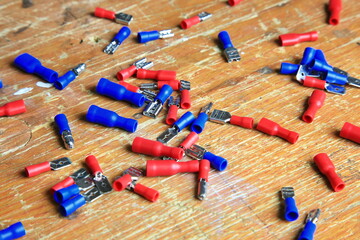 Verstreute rote und blaue isolierte Crimp- und Flachstecker mit sichtbaren Metallkontakten auf Holz; typische Komponenten f&uuml;r KFZ-, Elektrik- und Heimwerkerarbeiten.
