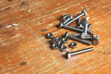 Edelstahl-Schrauben und Muttern auf verwitterter Werkbank, sichtbar Gewinde und Gebrauchsspuren, bereit f&uuml;r Montage- und Reparaturarbeiten.