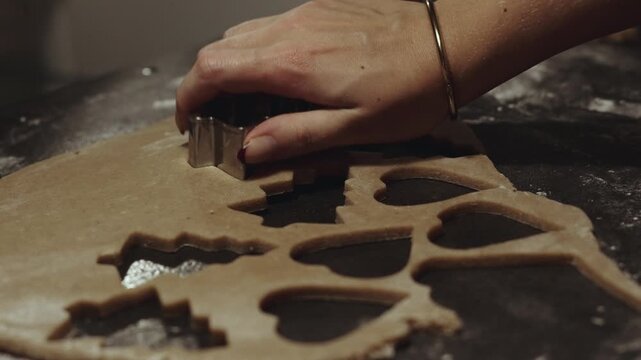 Female baker with christmas nails cutting cookie dough with cookie cutter, making christmas gingerbread cookies during family holyday baking day. Desaturated footage easily color matched
