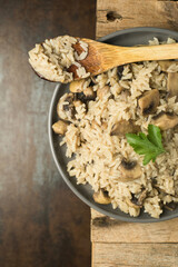 Cooking Rice with Mushrooms on a wooden table with a spoon and herbs
