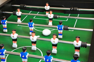 Kicker mit &Uuml;berraschung: Ein Ei liegt zentral auf dem gr&uuml;nen Spielfeld, flankiert von blauen und wei&szlig;en Kunststoffspielern auf Metallstangen; ungew&ouml;hnlicher, stiller Moment im Tischfu&szlig;ball.
