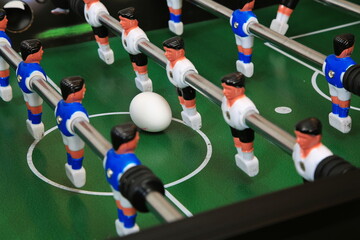 Kicker mit &Uuml;berraschung: Ein Ei liegt zentral auf dem gr&uuml;nen Spielfeld, flankiert von blauen und wei&szlig;en Kunststoffspielern auf Metallstangen; ungew&ouml;hnlicher, stiller Moment im Tischfu&szlig;ball.