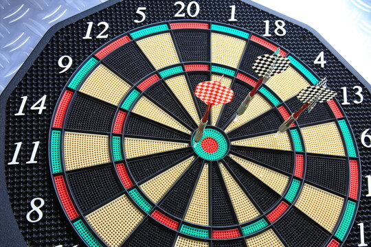 Drei Dartpfeile stecken pr&auml;zise in der Dartscheibe. Die kr&auml;ftigen Farben und der metallische Hintergrund betonen den Moment sportlicher Konzentration.