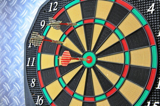 Drei Dartpfeile stecken pr&auml;zise in der Dartscheibe. Die kr&auml;ftigen Farben und der metallische Hintergrund betonen den Moment sportlicher Konzentration.
