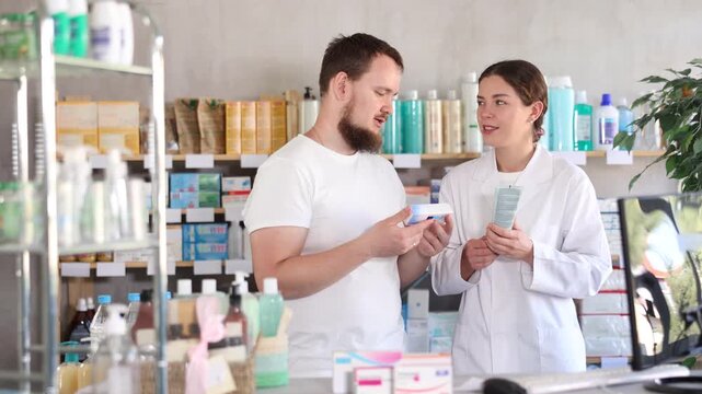 Man chooses ointment in modern pharmacy. Female pharmacist helps with choosing a medicine. High quality 4k footage