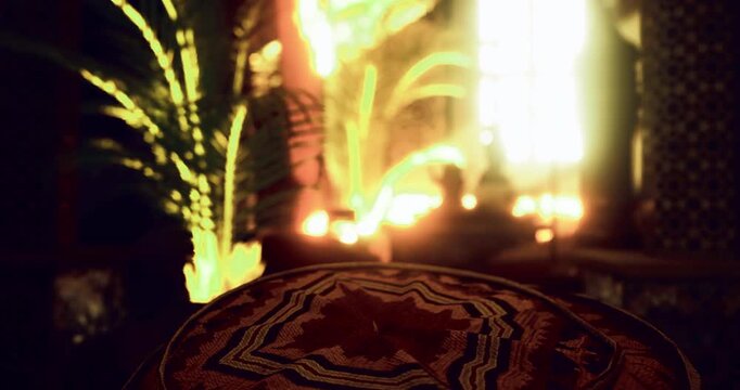 An inviting indoor area is showcased with colorful cushions placed on the floor. Ambient light pours in through the window, enhancing the rich cultural decor surrounding the space.