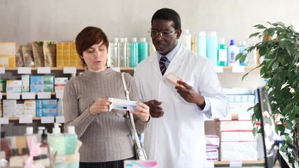 Woman choose buy gel for burns at pharmacy, compare with other good. Client check for absence of harmful substances, view product in details. African man pharmacist offer available assortment item