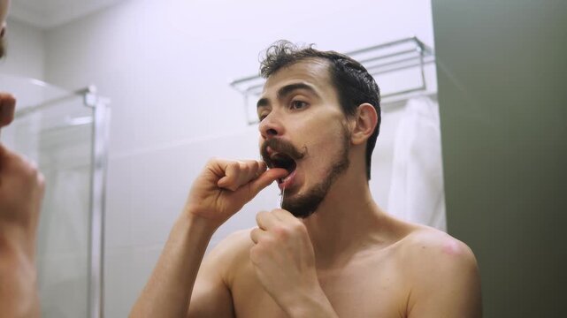 Man flossing confidently, Gentleman cleans teeth meticulously, Man in bathroom ensures perfect dental cleanliness, Caucasian man scrutinizes his smile during dental routine using precision techniques