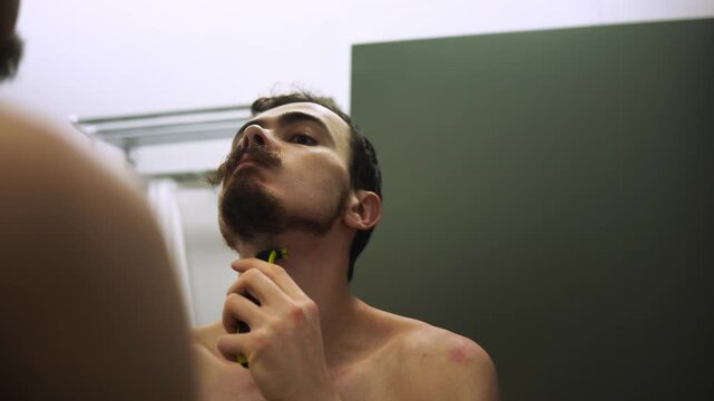 Man shaves attentively, Focused man preparing with grooming tools, Quiet evening scene of man shaving carefully, Neck shaving closeup showing concentration and grooming preparation for audition