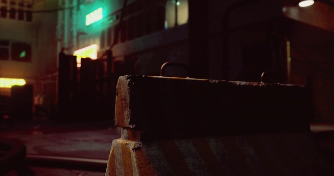 The urban alley features vibrant neon lights reflecting off wet surfaces. Construction materials sit prominently in the foreground, capturing the moody atmosphere of the nighttime setting.