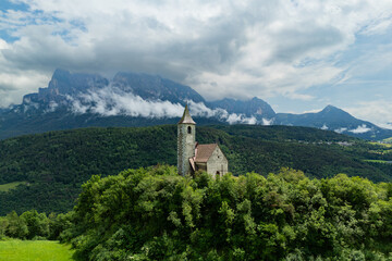 Fototapeta premium St. Andreas bell tower on a hilltop clearing bordered by woodland, aerial view. Northern Italy countryside