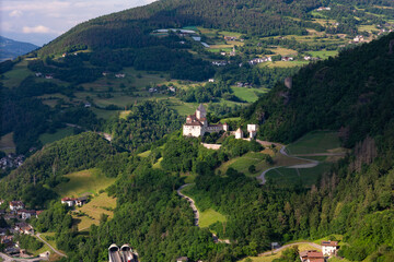 Fototapeta premium Trostburg Castle above rural settlements on a wooded slope, aerial view. Medieval architecture in South Tyrol, Italy