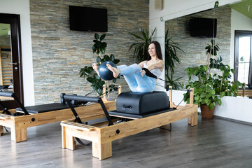 A woman demonstrates Pilates exercises on a reformer machine, showcasing strength and balance, set...