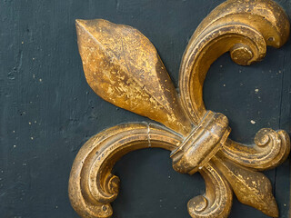 Golden fleur de lis ornament on dark wooden surface © Enigma