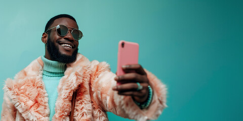 African American man in stylish fur coat taking selfie with smartphone against teal background