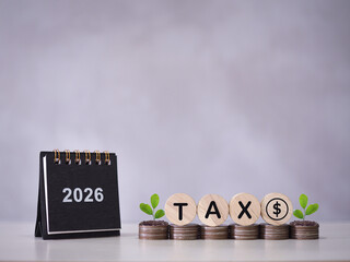2026 desk calendar, Wooden blocks with the word TAX and plants growing up on stack of coins. The concept about saving money and manage time to paying tax in year 2026
