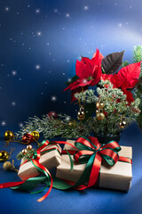 Christmas decor with handmade gift boxes, poinsettia, decorative fir branch, bells and balls for tree decoraton on blue vertical background with shining star. Winter holiday composition with presents.
