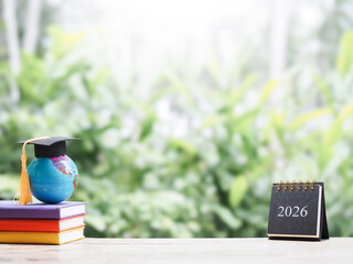 Student creative desktop, Earth globe with graduation hat on hardcover book and 2026 desk calendar. Copy space for text, Back to school, Education concept